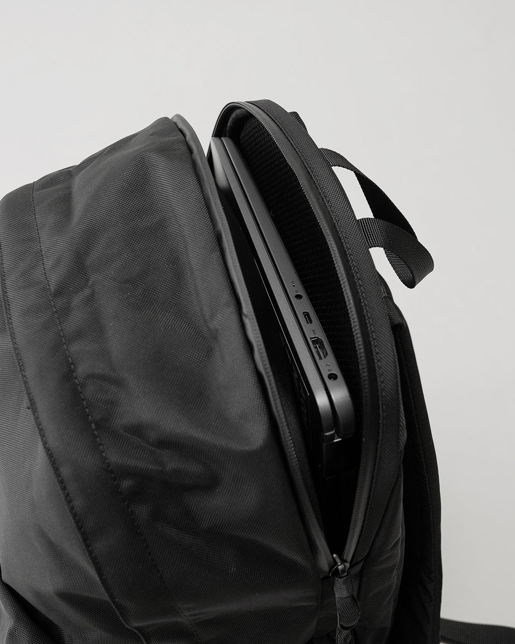 LC Daypack STANDARD 16Lのメイン画像。黒色のバックパックを斜め上部から撮影し、ジッパー付きポケットと持ち手が見える前面ディテール}