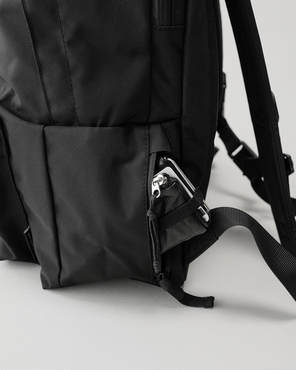 LC by LOWERCASE の DAYPACK STANDARD 16Lの側面。黒の丈夫なナイロン素材で、サイドポケットとジッパー付きポケットのディテールが見える。ショルダーストラップと背面の構造も一部見える。