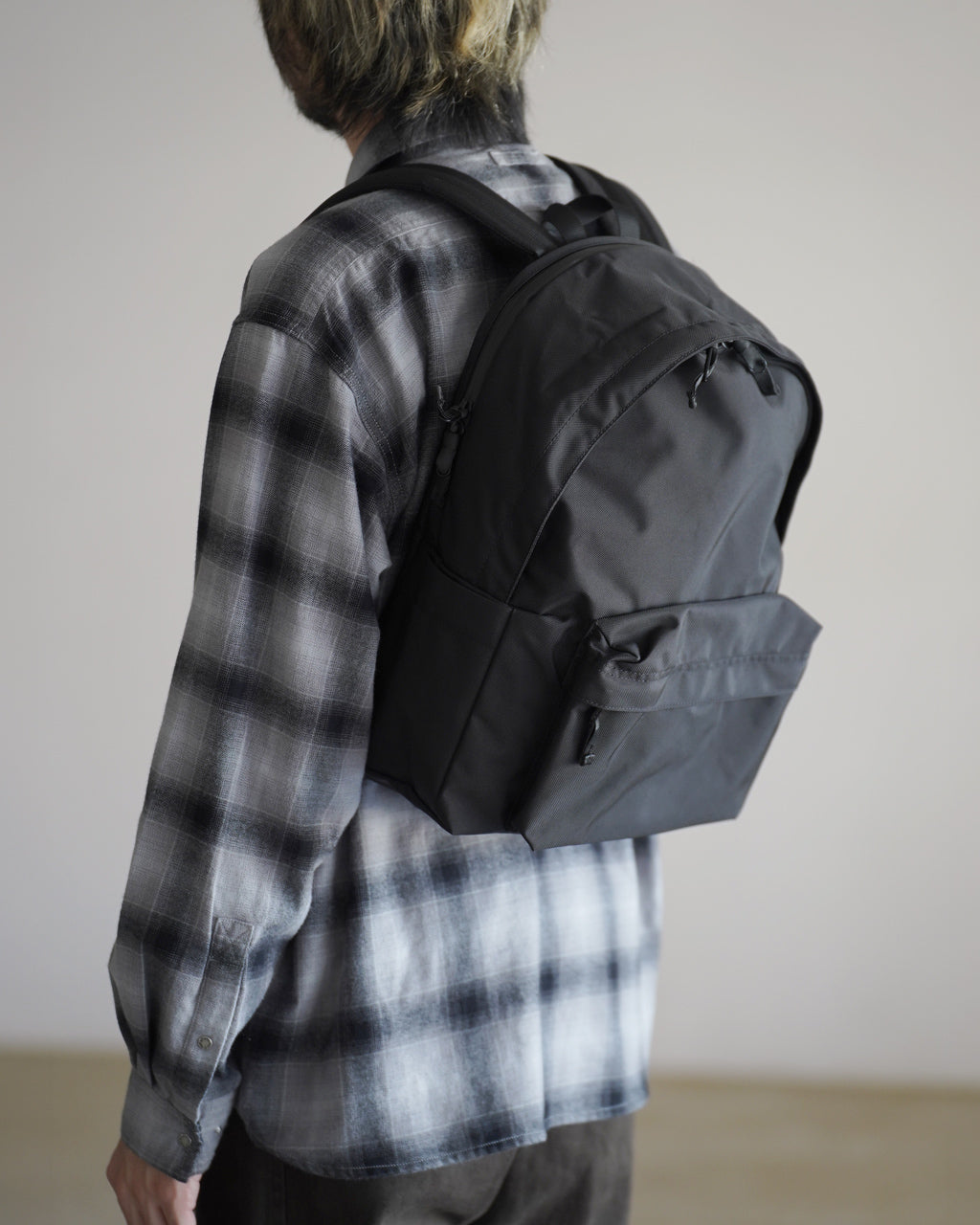 LC by LOWERCASEのバックパック STANDARD 16Lの着用イメージ。黒系の落ち着いたカラーで、前面ポケットと側面ポケットを備えたシンプルなデザインです。
