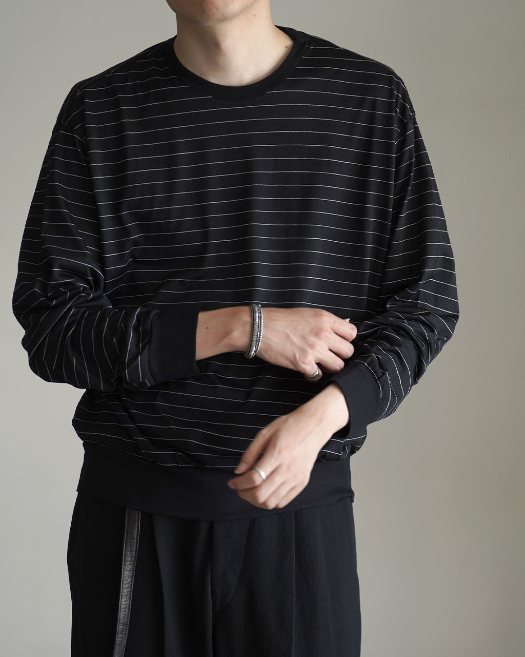 ブラック系ボーダーのクルーネック長袖Tシャツ。細い横ストライプが全体に入ったリラックスシルエットで、袖口と裾はリブ仕様。