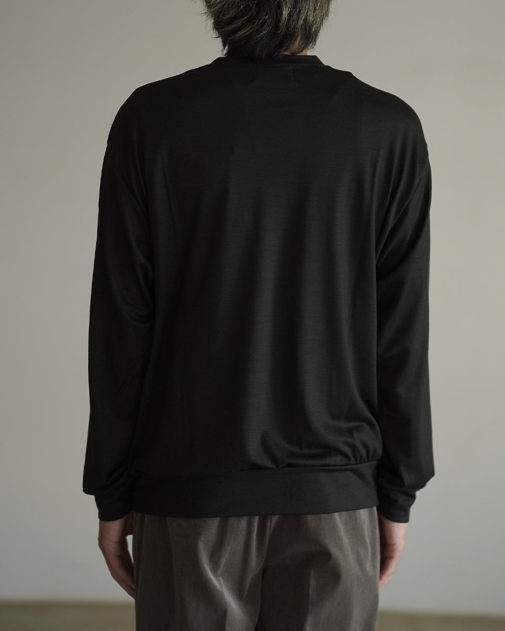 背面から撮影された黒のロングスリーブTシャツ。襟元はスリムなクルーネックで裾はリブ仕様、体に沿うシルエットが特徴的。