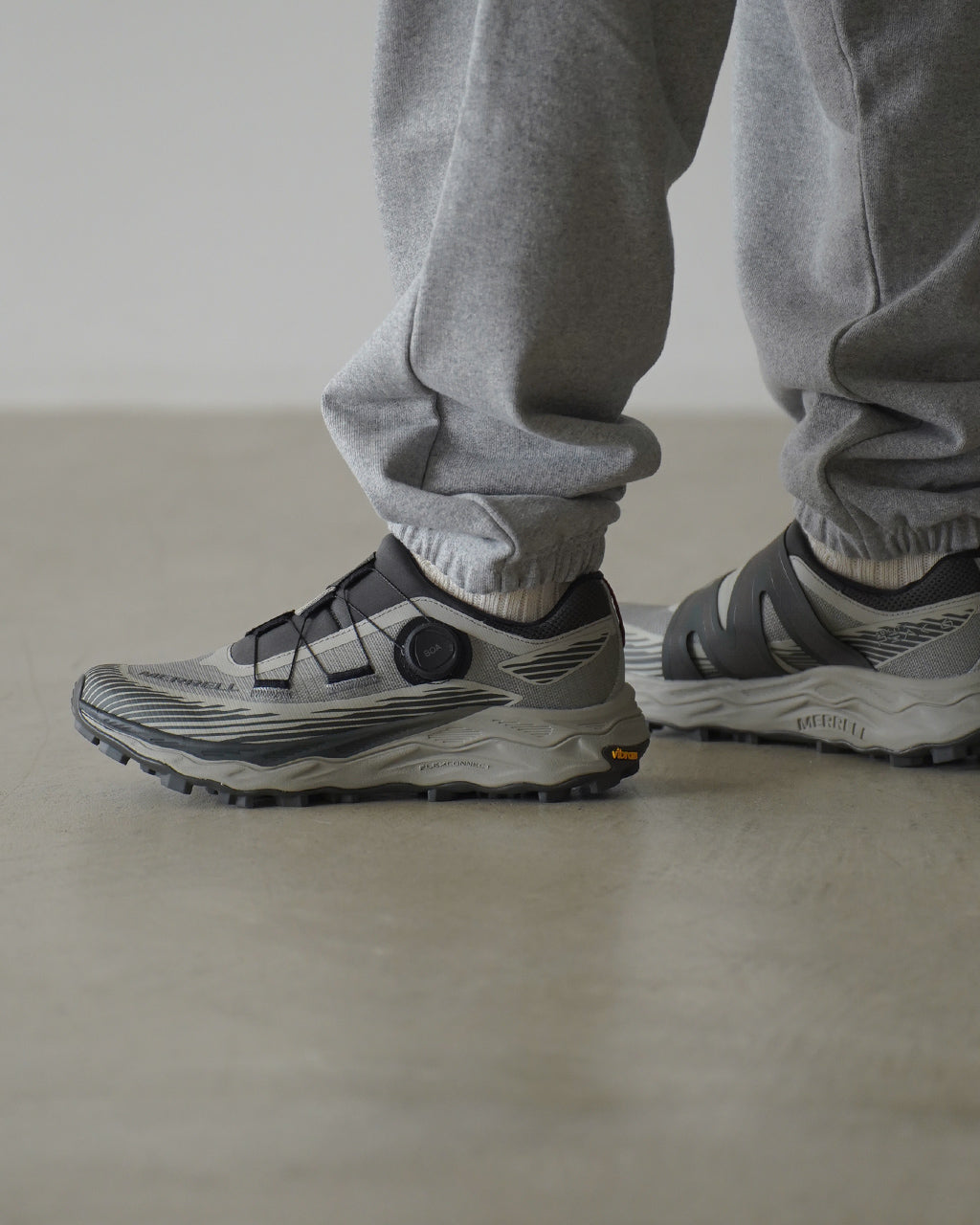 MERRELL AGILITY PEAK 6 BOA の側面とつま先部分が見える着用イメージ。グレー系のアッパーと厚みのあるソール、BOAダイヤルが配置されたデザインを表示