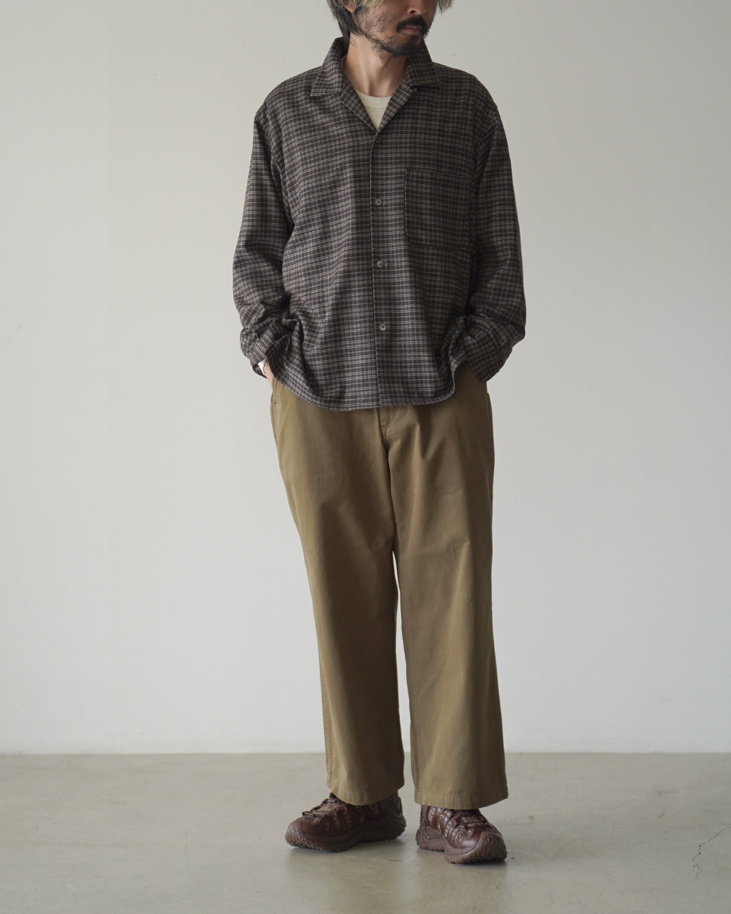 ダークウッド系のチェック柄シャツを着た男性モデルの全身。パンツはカーキ色のワイドストレート。足元はブラウンのトレッキングシューズを組み合わせたカジュアルなスタイル