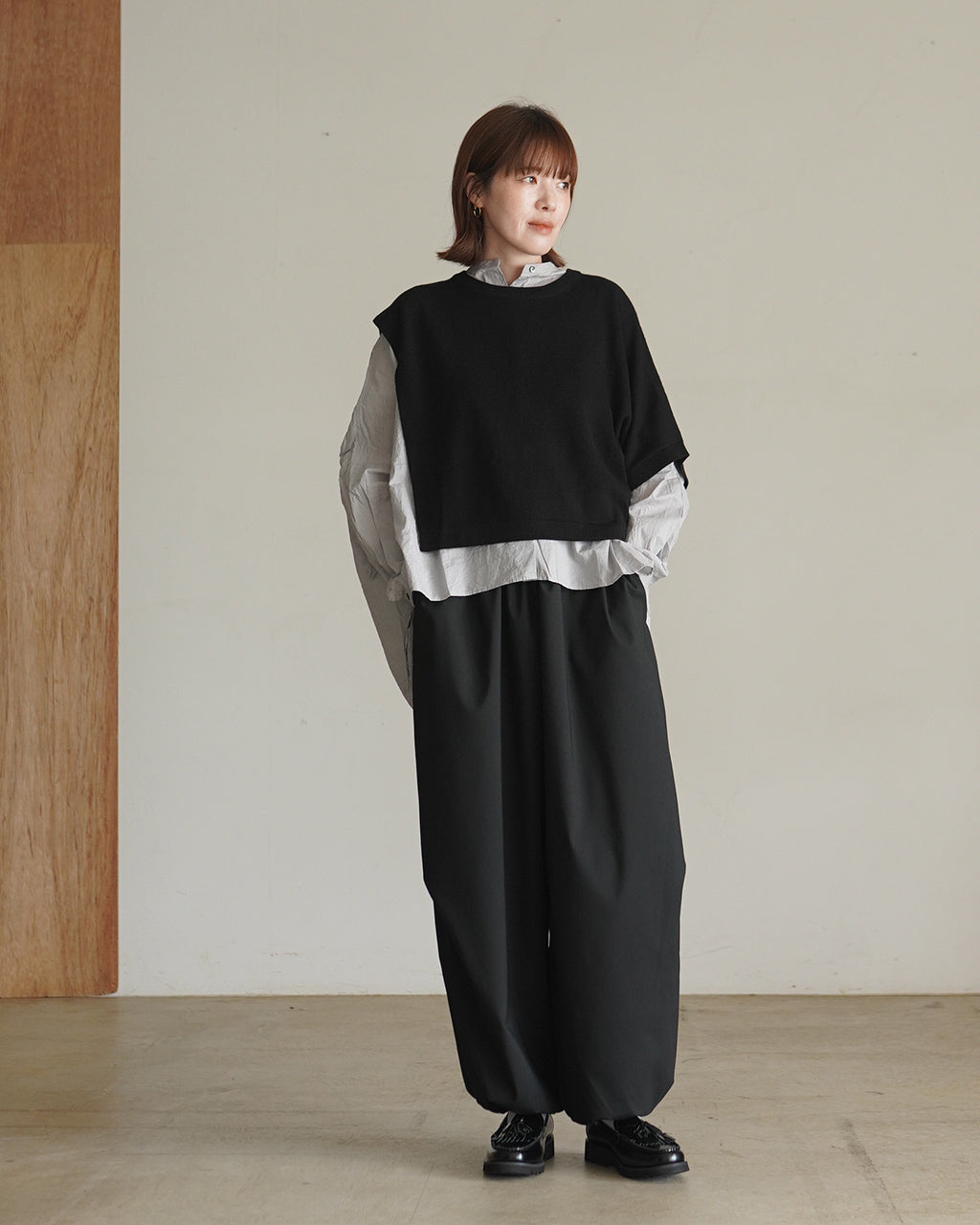 黒のアシンメトリーニットの下に、白いシャツを合わせた着こなし。肩の落ちたドロップショルダーとクロップド丈が特徴的なアイテム画像。