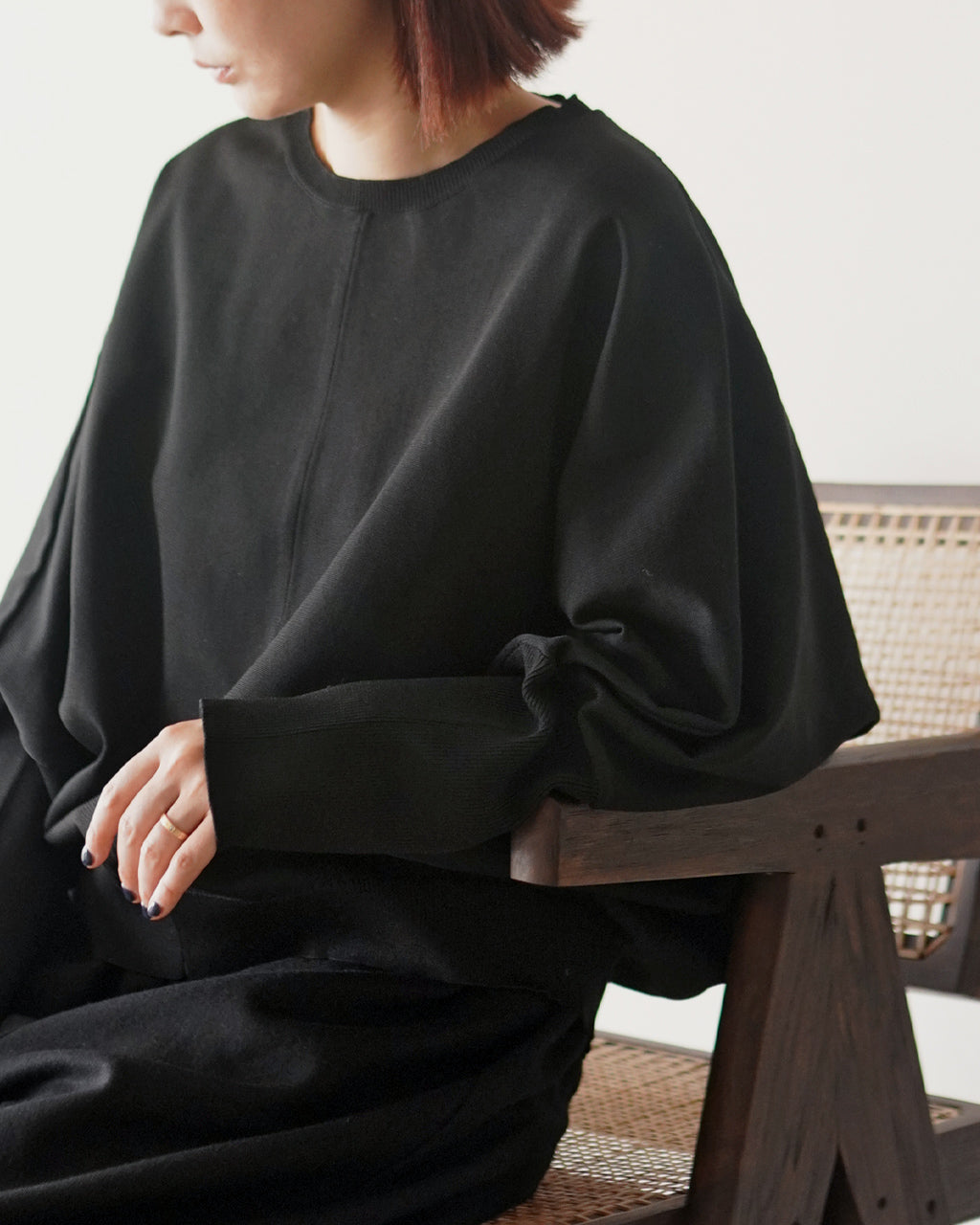ミズイロインドの cocoon P/O を着用したモデルの横からのアップ。ゆったりとしたビッグシルエットのクルーネックと長めのドルマンスリーブが特徴的なブラックのニット全体像。
