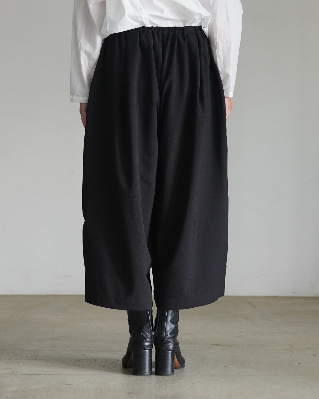 腰下までゆったり落ち着いたシルエットの黒いワイド半パンツ。ウエストはゴム仕様で着用感が楽そうなデザイン、裾は少し広がる長め丈で足元をすっきり見せます。