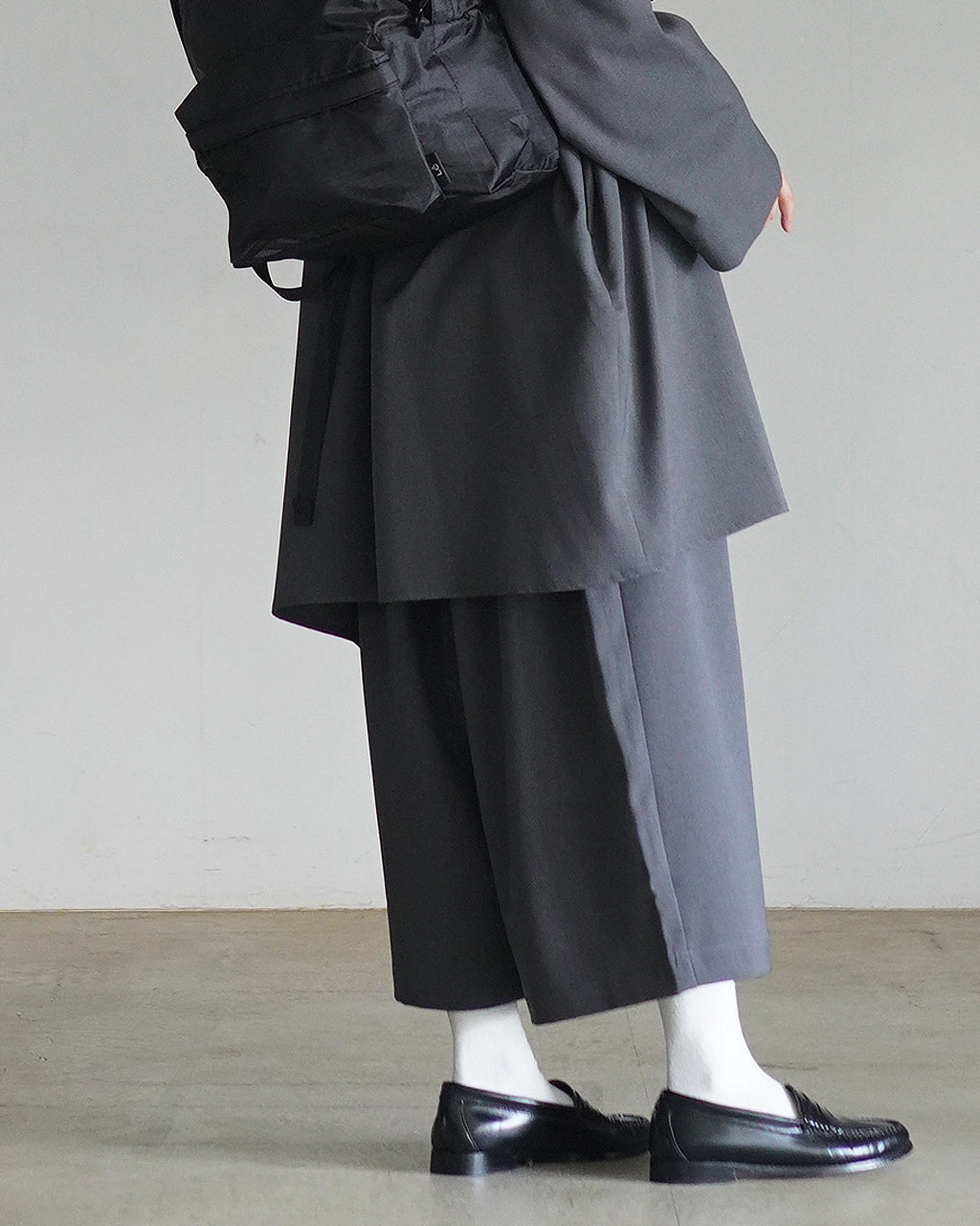 黒のワイド半端パンツを着用したモデルの横姿。膝下まで落ちるゆとりのあるシルエットと、裾へ向かって広がるデザインが見える。