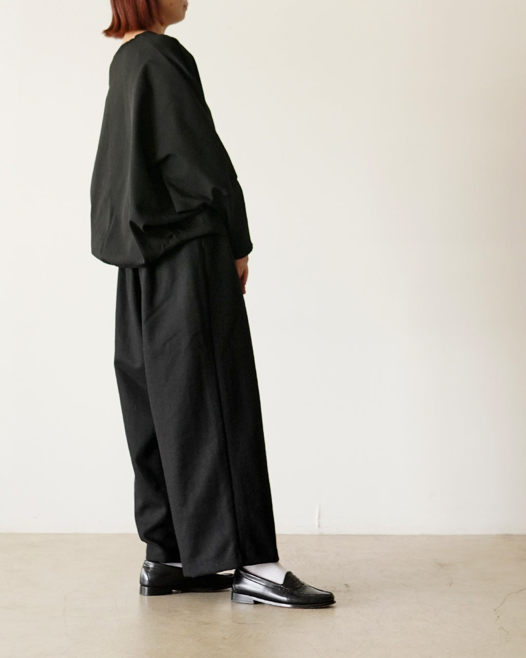 黒系のワイドパンツを着用した女性の横姿。ゆったりとしたシルエットと裾まで落ちるラインが特徴的。足元は黒のローファーを合わせ、全体に落ち着いた印象。