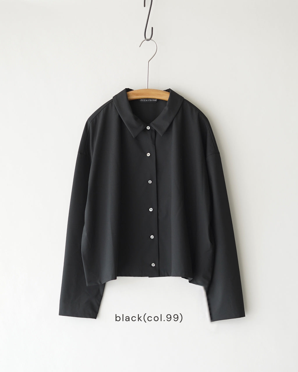 mizuiro indのブラック系シャツ。前立てに白いボタンが並び、すっきりとした長袖の定番デザイン。干し布に掛けられた状態で、首元はクラシックな裏地のない襟元を見せる