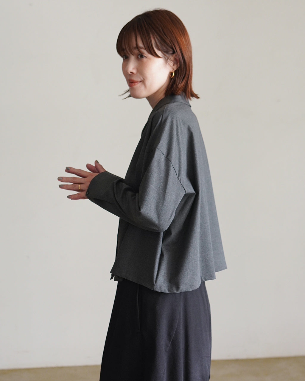 mizuiro indのグレー系ワイドシャツを着用した女性のサイドショット。ゆるやかなドロップショルダーと長めの袖口が特徴的。カジュアルな雰囲気の前後差のあるシルエット