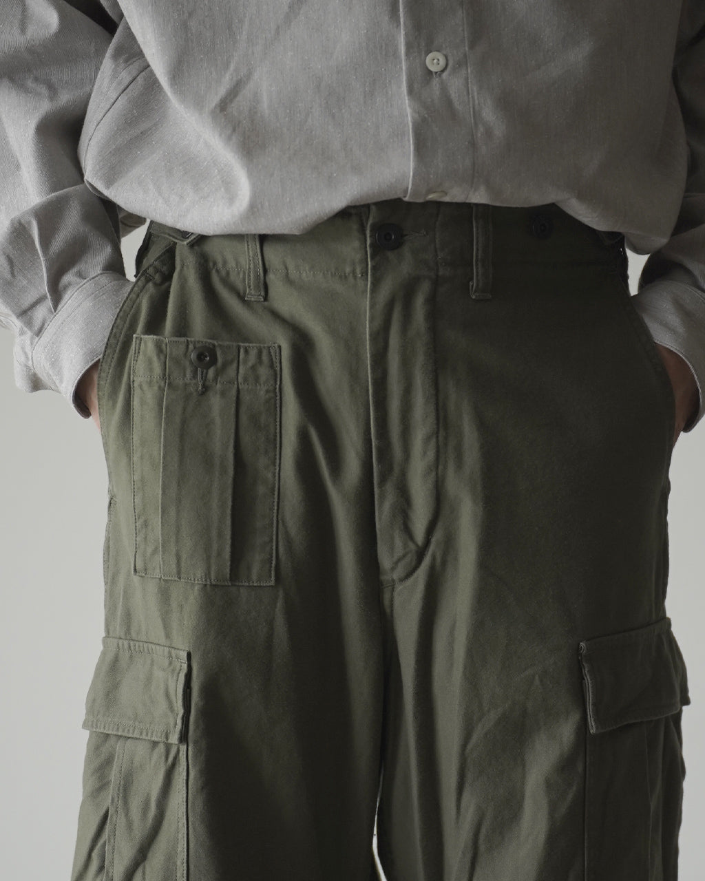 ナイジェル・ケーボンのARMY CARGO PANTを腰元から撮影。濃緑色のカーゴパンツとベージュ系シャツの組み合わせで、ウエスト周りと大きなカーゴポケットが強調されています。