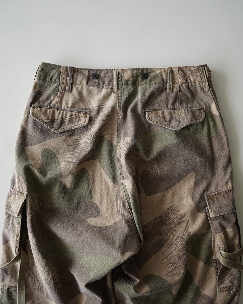 迷彩柄のARMY CARGO PANTの後ろ姿。腰帯とベルトループ、カーゴポケットのバックスタイルが特徴的なカーゴパンツ。