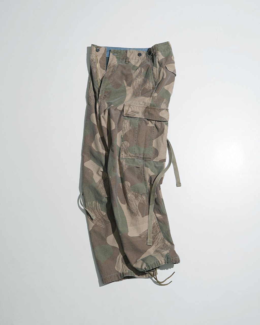 フェードカモ柄のARMY CARGO PANTの横から見たカーゴパンツ、スリット付きポケットとドローコードが特徴的なミリタリースタイル