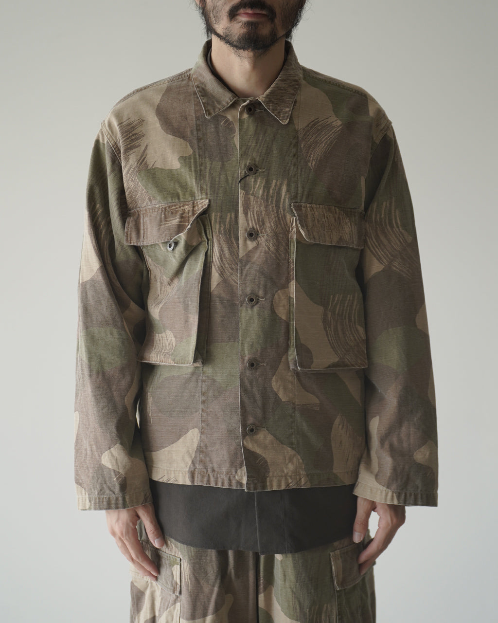 ナイジェル・ケーボンのFIELD JACKET FADE CAMOの正面ショット。カモフラ柄が全面に入り、前面ポケットのフラップが際立つジャケット姿。