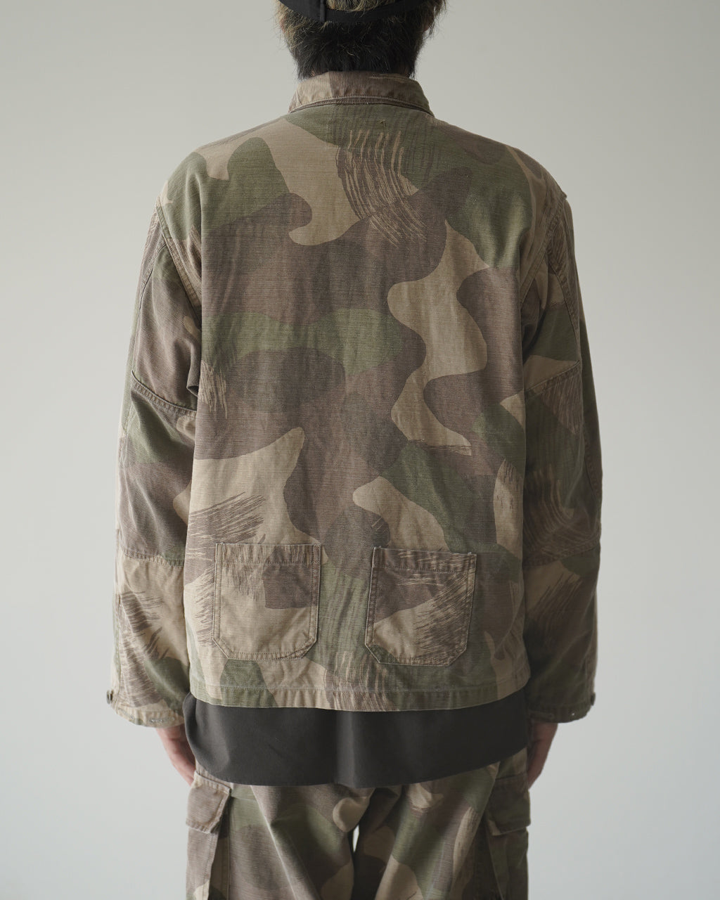 背面に迷彩柄が広がるFIELD JACKET FADE CAMO。カバー付きのポケットが2つ、裾まで届くやや長めの丈感が特徴。