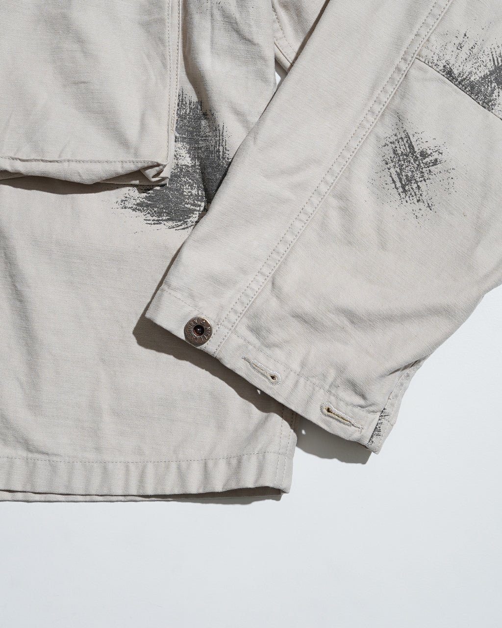 ナイジェル・ケーボンのFIELD JACKET FADE CAMOを撮影した前面の一部。淡いベージュ系ボディにカモフラージュ柄のプリントと袖口のボタンが見えるショット