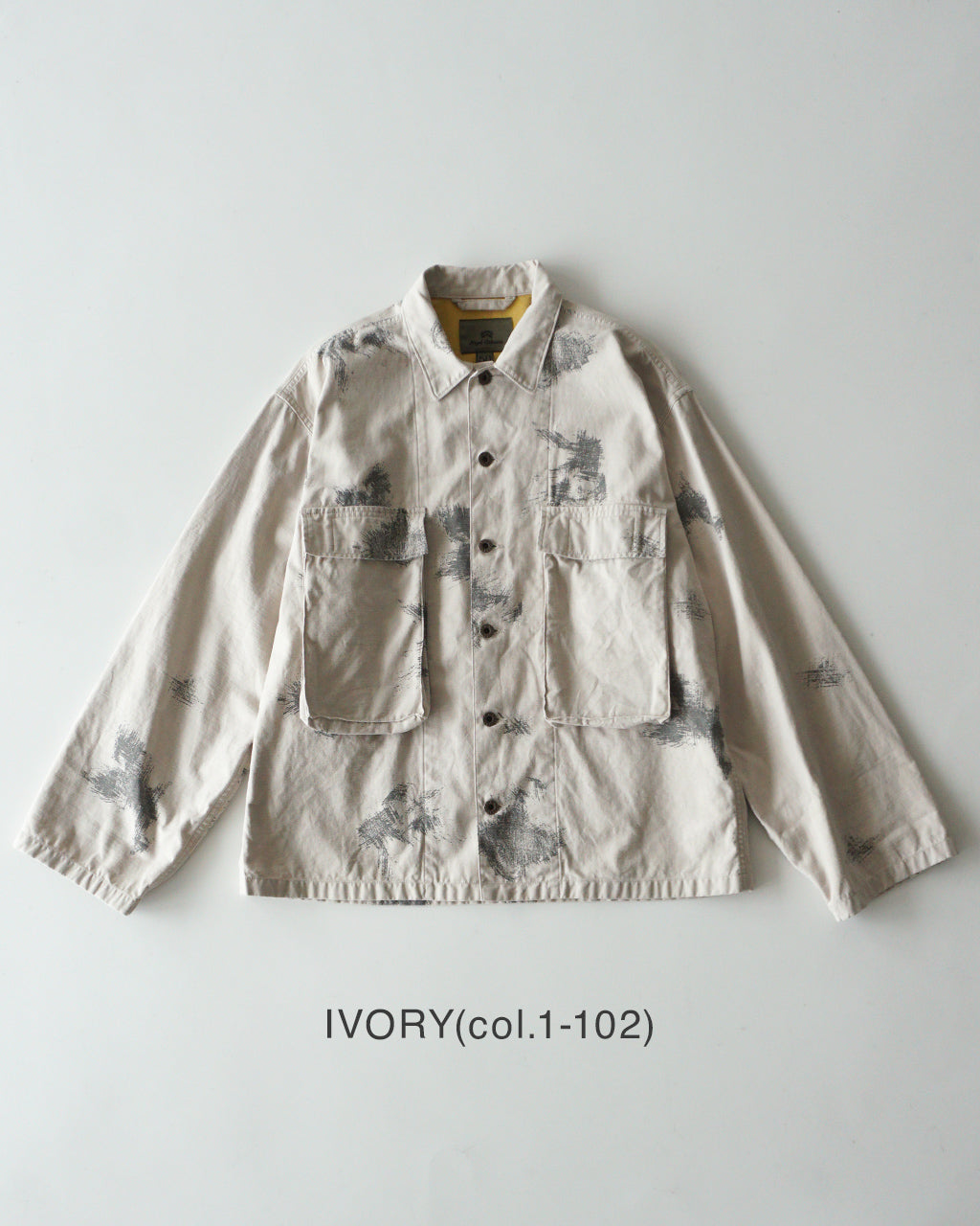 アイボリー系の_field jacket_ fading camoデザイン。前面は胸ポケット付き、両サイドにも大型ポケットが配され、肩と袖にカモ柄のプリントが部分的に見える。背面は表示なし。