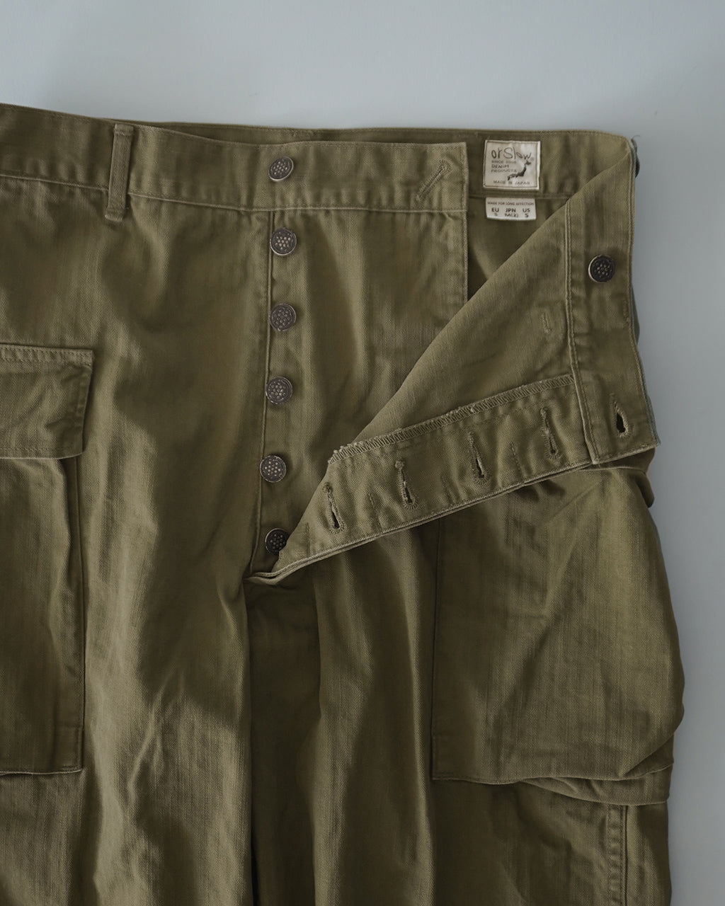 カーキ色のU.S ARMY 2 POCKET CARGOパンツのウエスト周りと前開き部分。フロントボタンと大きめのカーゴポケットが見えるデザイン。
