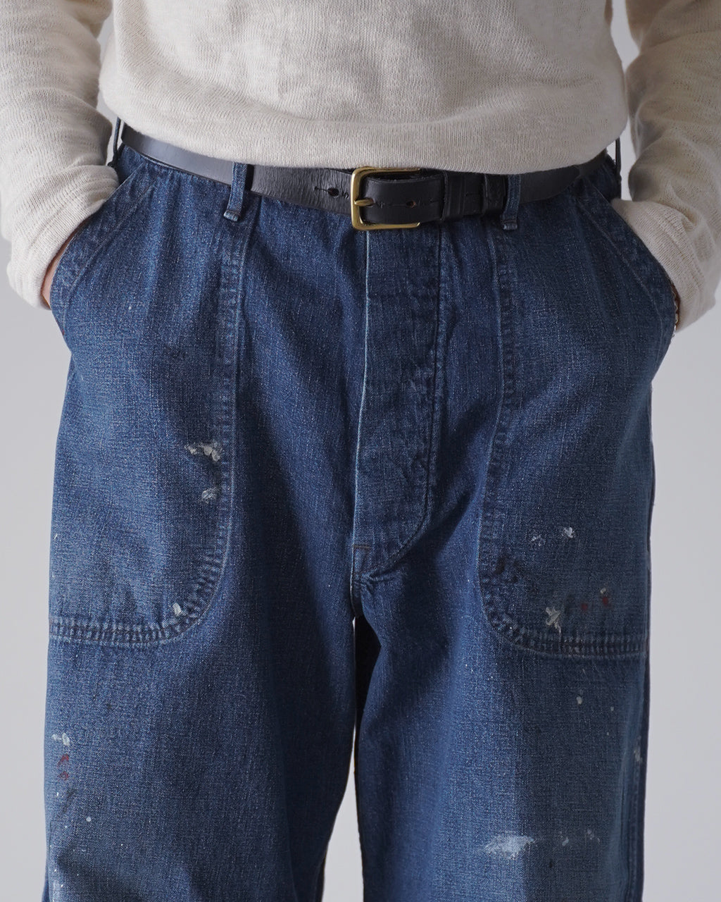 ベルト付きウエストのワイドストレートデニムパンツ。ネイビーの色味と淡いペイント風のダメージ加工が特徴的で、前ポケットが見える着用イメージ。