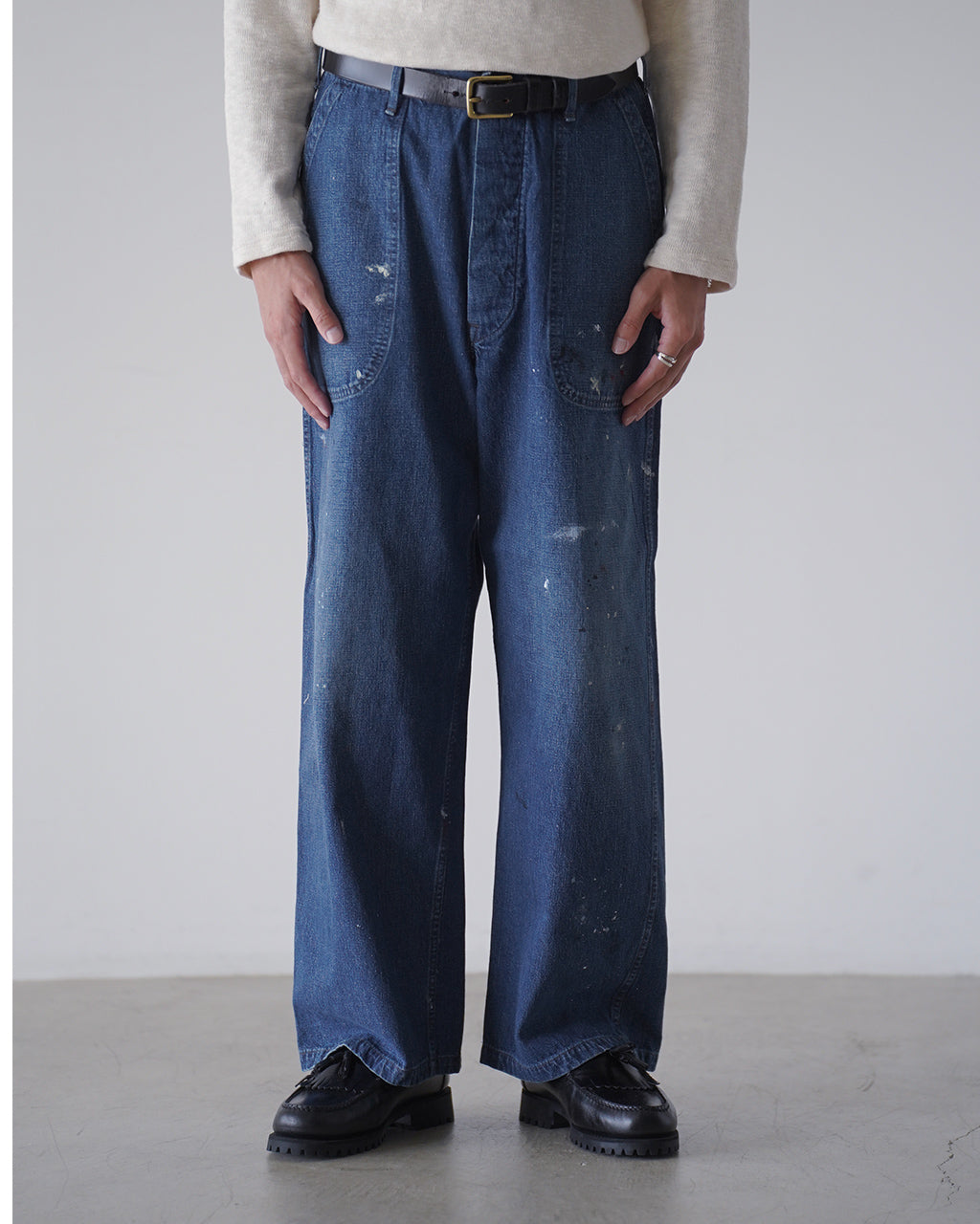 indigoデニムの幅広ストレートパンツ。前面には大きめのパッチポケット、裾に向かってやや広がるシルエットが特徴。薄い色落ちやペイント風のプリント跡がヴィンテージ感を演出。