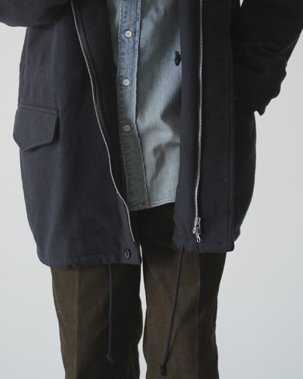 前はフロントジップとボタンが見えるコート。ダークネイビーの素材に denim シャツ風のインナーをレイヤードした着こなしの一枚。