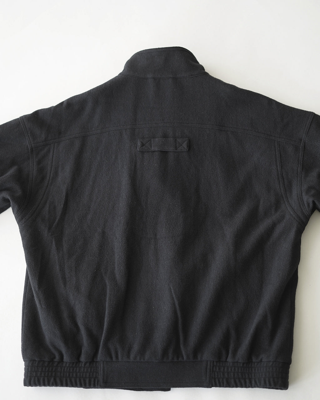黒系のVESTE ABOS OV-T055の背面ショット。スタンドカラーと特徴的な後ろポケットのディテールが際立つ。裾はリブ仕様で絞り感があるデザイン。