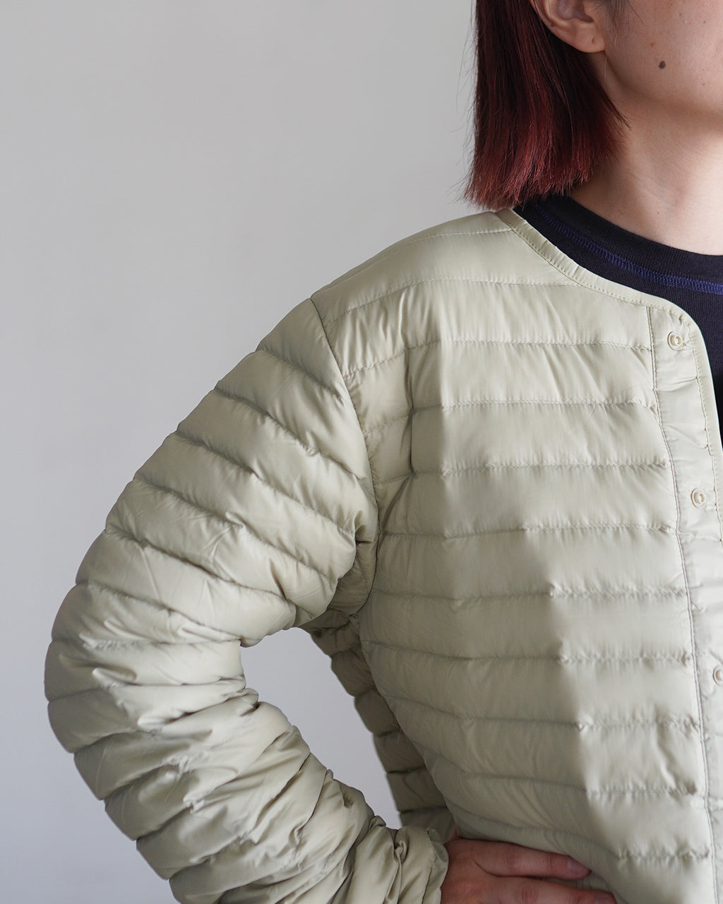 ライトベージュのパデッドジャケットを斜め前から。肩まわりや横のシームが連なる quilting が特徴。前面はボタン留めで、薄手ながら保温性を感じるデザインです。