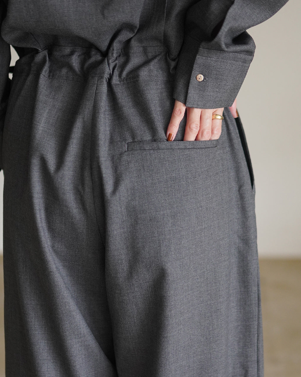 グレー系のFine Worsted Jumpsuitのウエスト周り。パンツの後ろポケットと生地の落ち感、袖口のボタンが見えるディテール写真