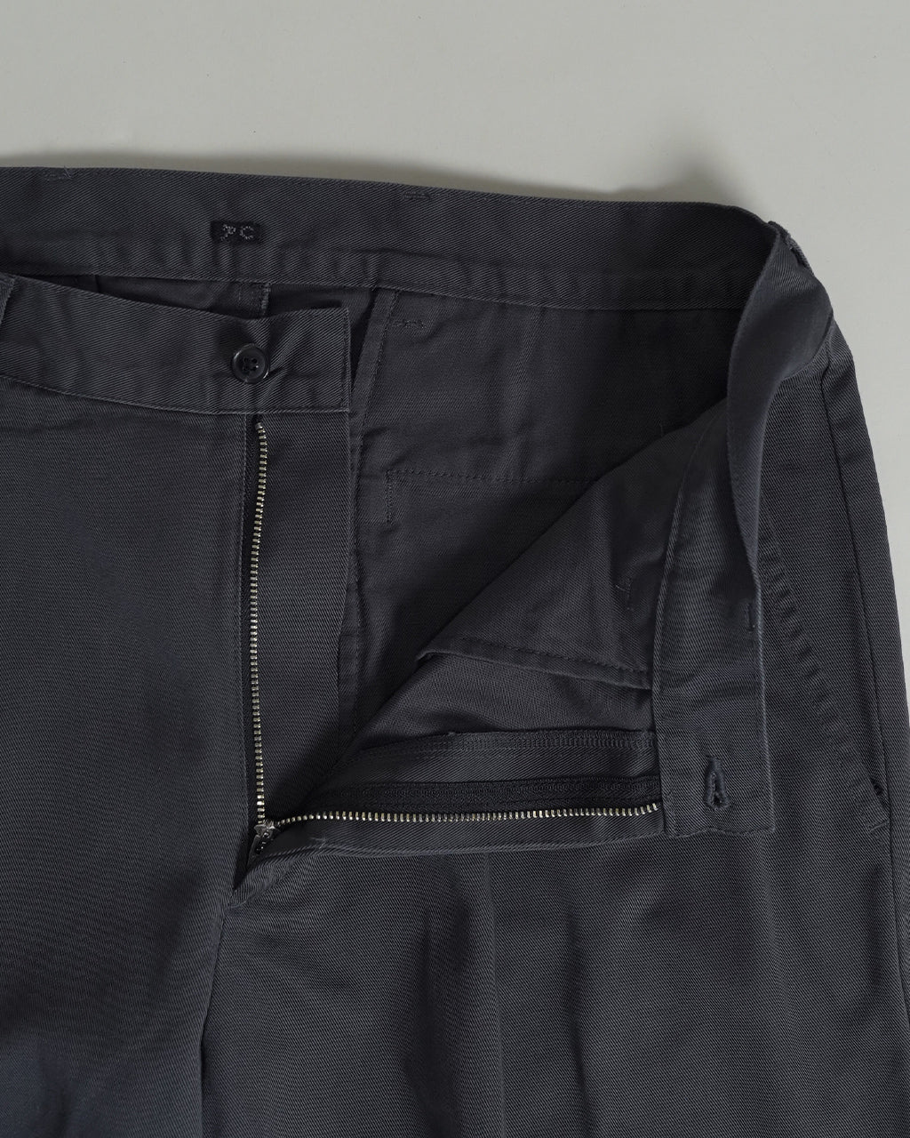 PORTER CLASSICのDuke Ellington Chinosの前開きファスナーと腰回りのタックが見えるグレー系パンツの内側ディテール。ジッパーとボタン留めの仕様が近接で確認できる
