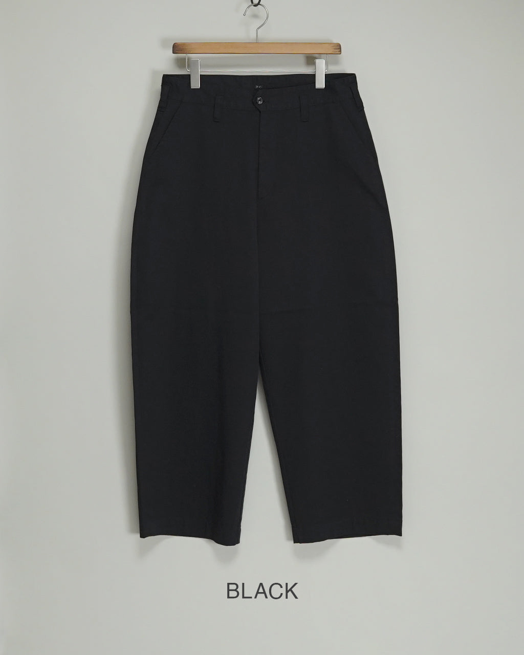 PORTER CLASSICのGENE KELLY CHINOSを前から吊り下げハンガーに掛けた状態。ブラックカラーのストレートなシルエットで、ウエスト周りのディテールと裾に向かう緩やかなテーパードが見える。