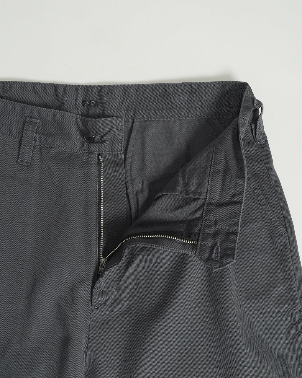 PORTER CLASSIC の GENΕ KELLY CHINOS の前部はズボンの前開きファスナーとジップが露出。濃いグレー系のコットン生地で、ポケット周りの縫い目が見えるデザインです。