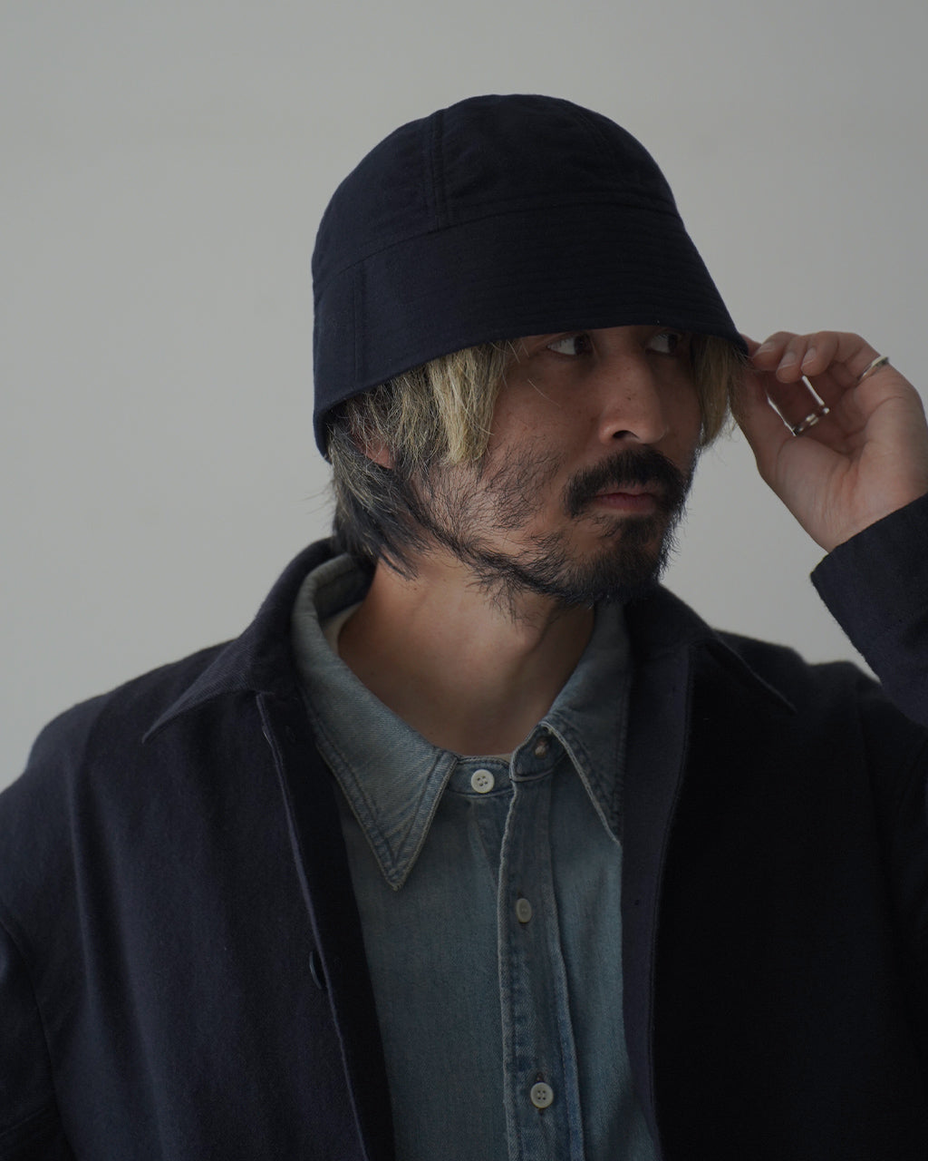 深いネイビーのロングブリムハットを着用した男性のアップ。モールスキンの質感と深いフォルムが特徴で、頭部をしっかり覆うデザインが印象的です。
