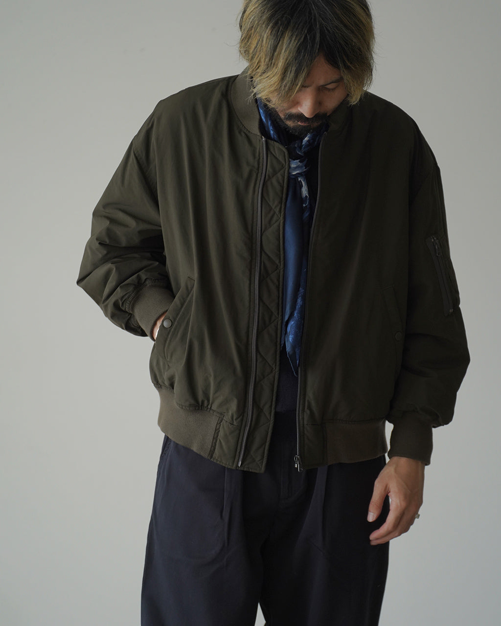 オリーブカラーの WEATHER FLIGHT JACKET が前から撮影され、ジップとリブ付きの袖口、ポケットディテールが見える。柔らかな質感の生地とゆとりのあるシルエットが特徴的。