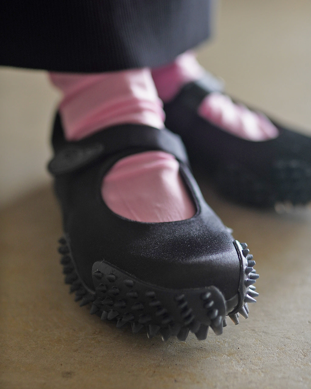 ブラックのPUMA Mostro Fey Satinを寄りで捉えた足元。丸みのあるつま先とストラップ、突起のあるソールが見える