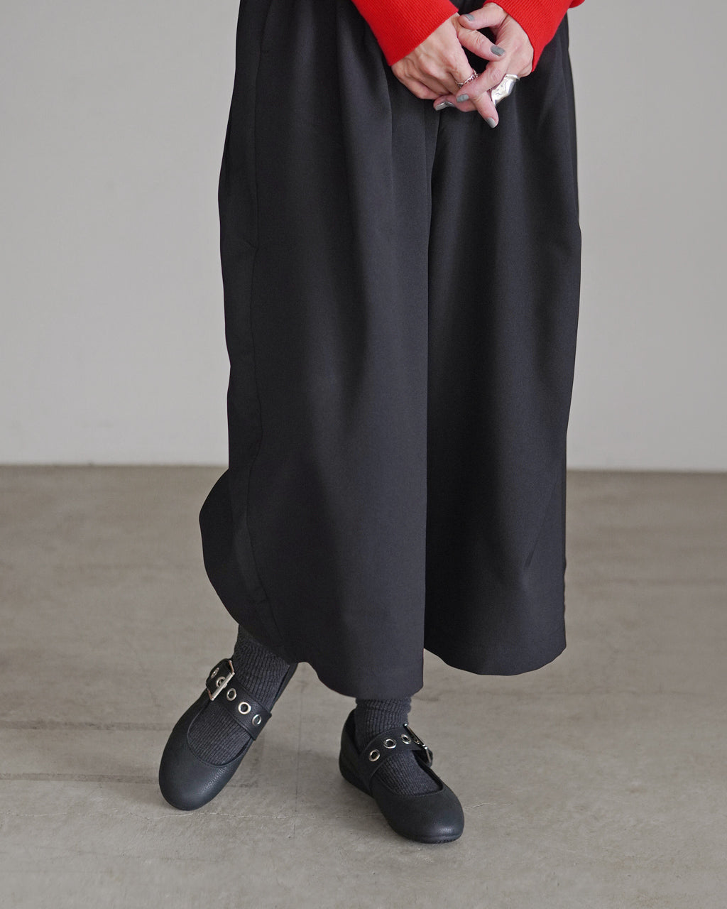 黒の長めスカート風パンツに赤いトップスを合わせ、足元は黒のフラットシューズとソックスを着用した女性の下半身ショット