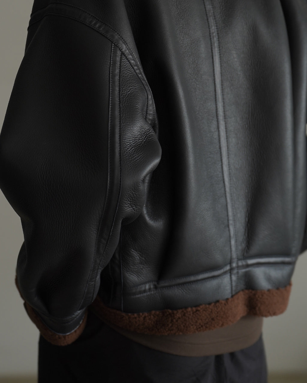 ブラックのムートンレザー素材で作られたPLEATED AVIATOR JACKETの袖とサイドをクローズアップ。質感の細かな皺と、裾のボアライニングが映えるディテールショットです。