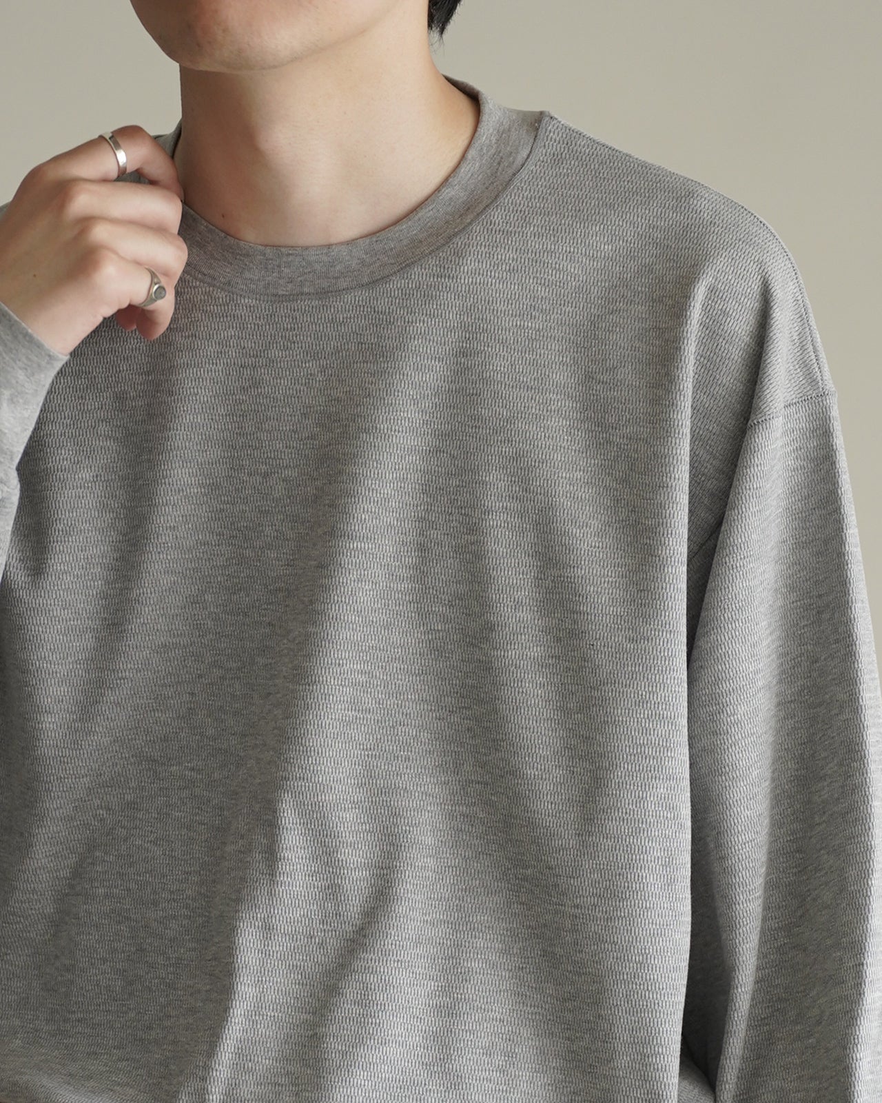 グレー系の長袖Tシャツ。細かなリブ編み生地で、首元は丸首。袖口のプリーツが立体感を生み、胸元や背中のシルエットはすっきりした印象です。