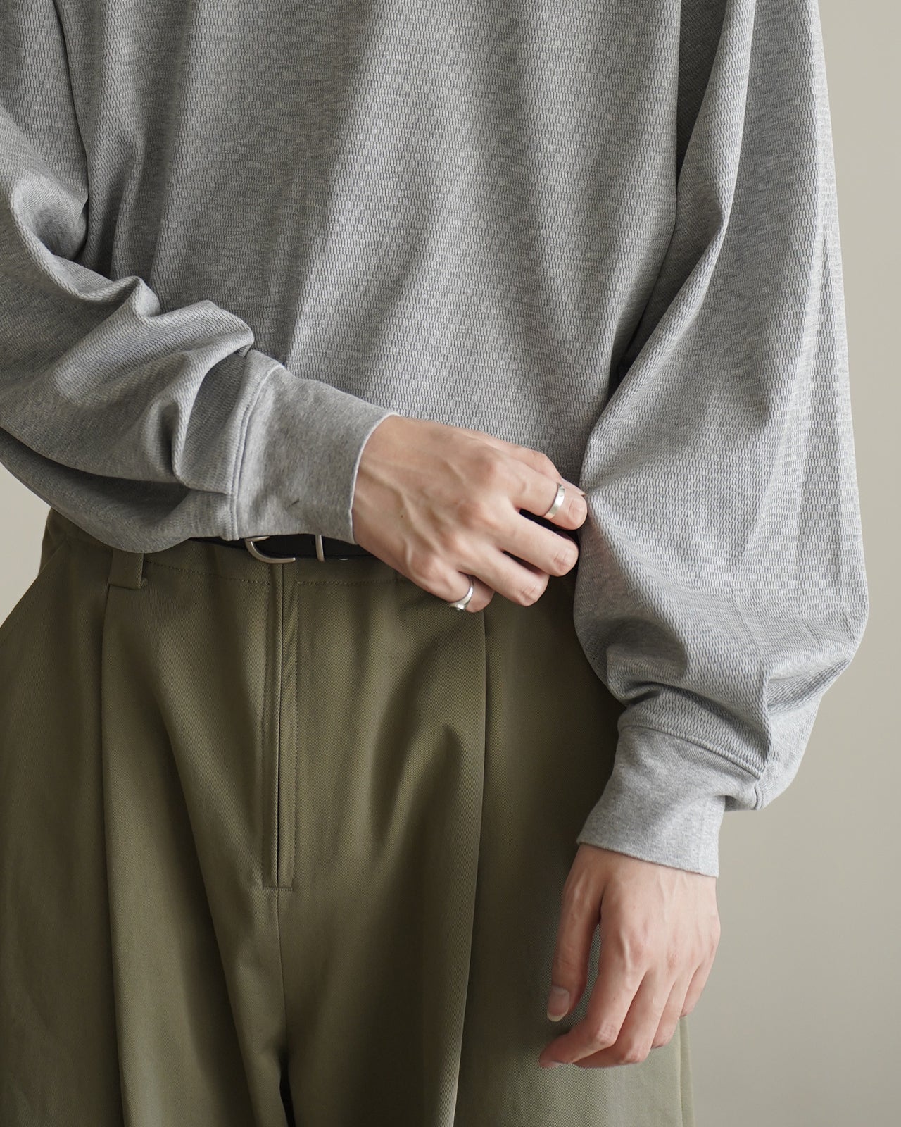 グレーのサーマル長袖Tシャツの正面ショット。やや光沢感のある生地と立体的な編み目、袖口のプリーツが目立つデザイン。