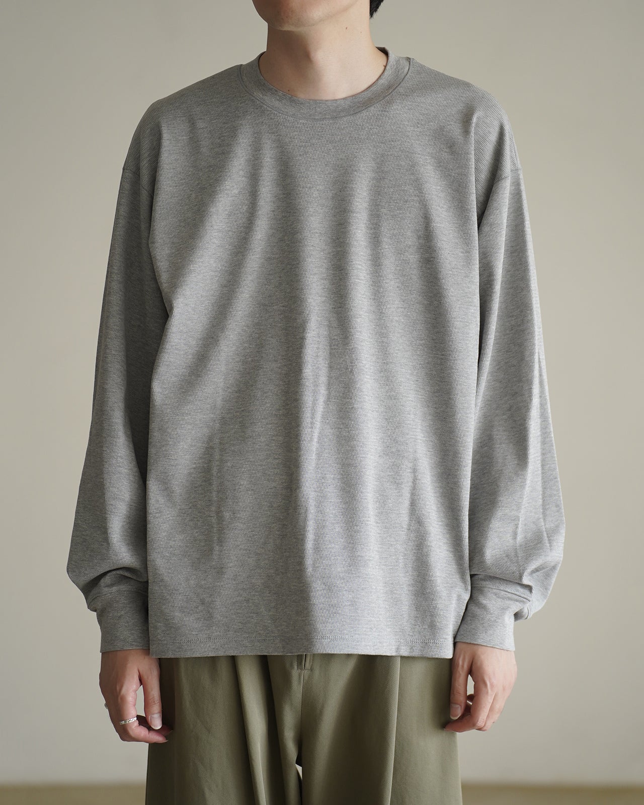 グレーのロングスリーブTシャツ。綿100%のサーマル生地で、袖口のプリーツが立体感を表現。ゆったりとしたシルエットで首元はラウンドネック。