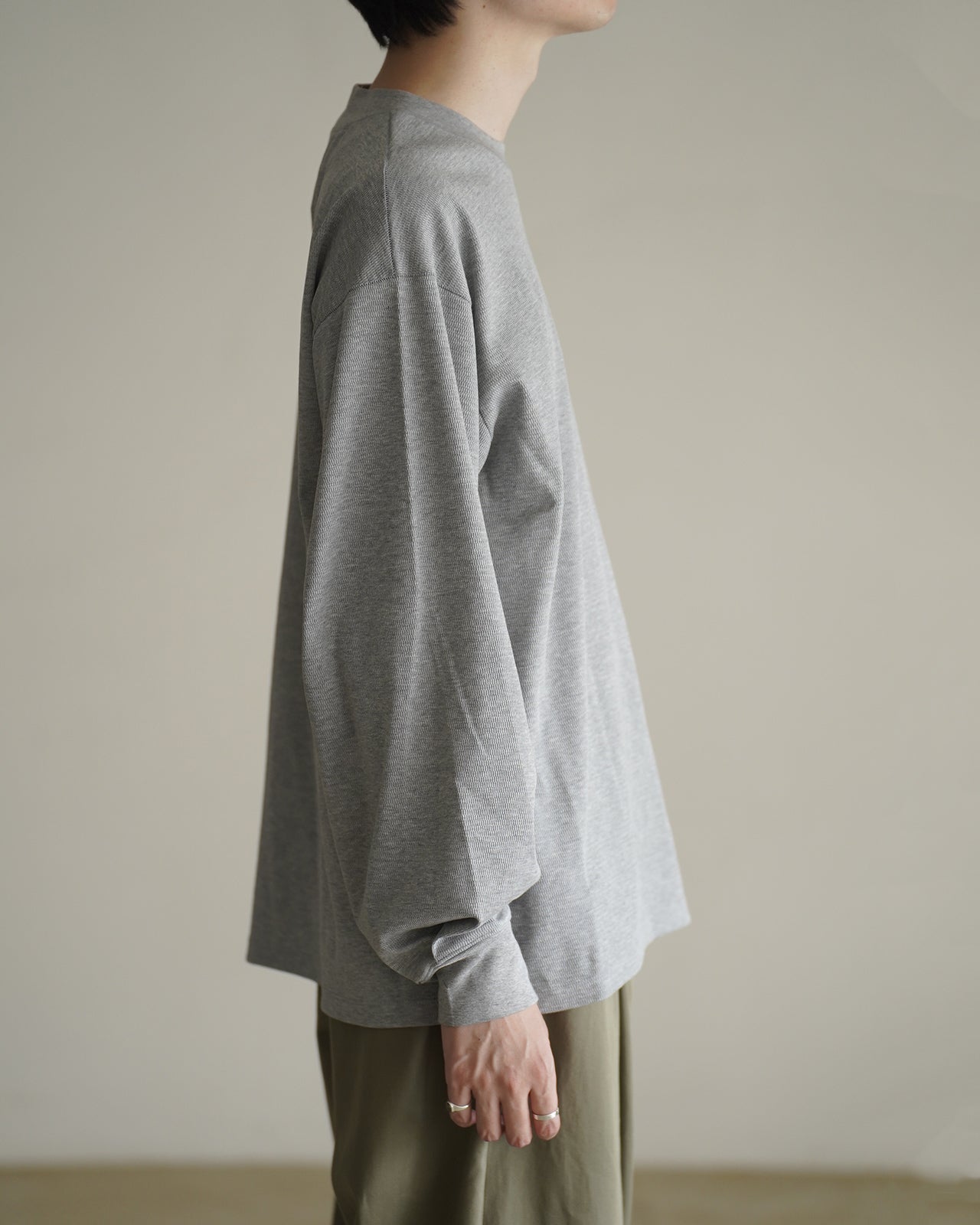 グレーの長袖Tシャツの横からのシルエット。袖口に適度な余裕があり、ややゆったりとしたリブ生地の質感が伝わる写真。
