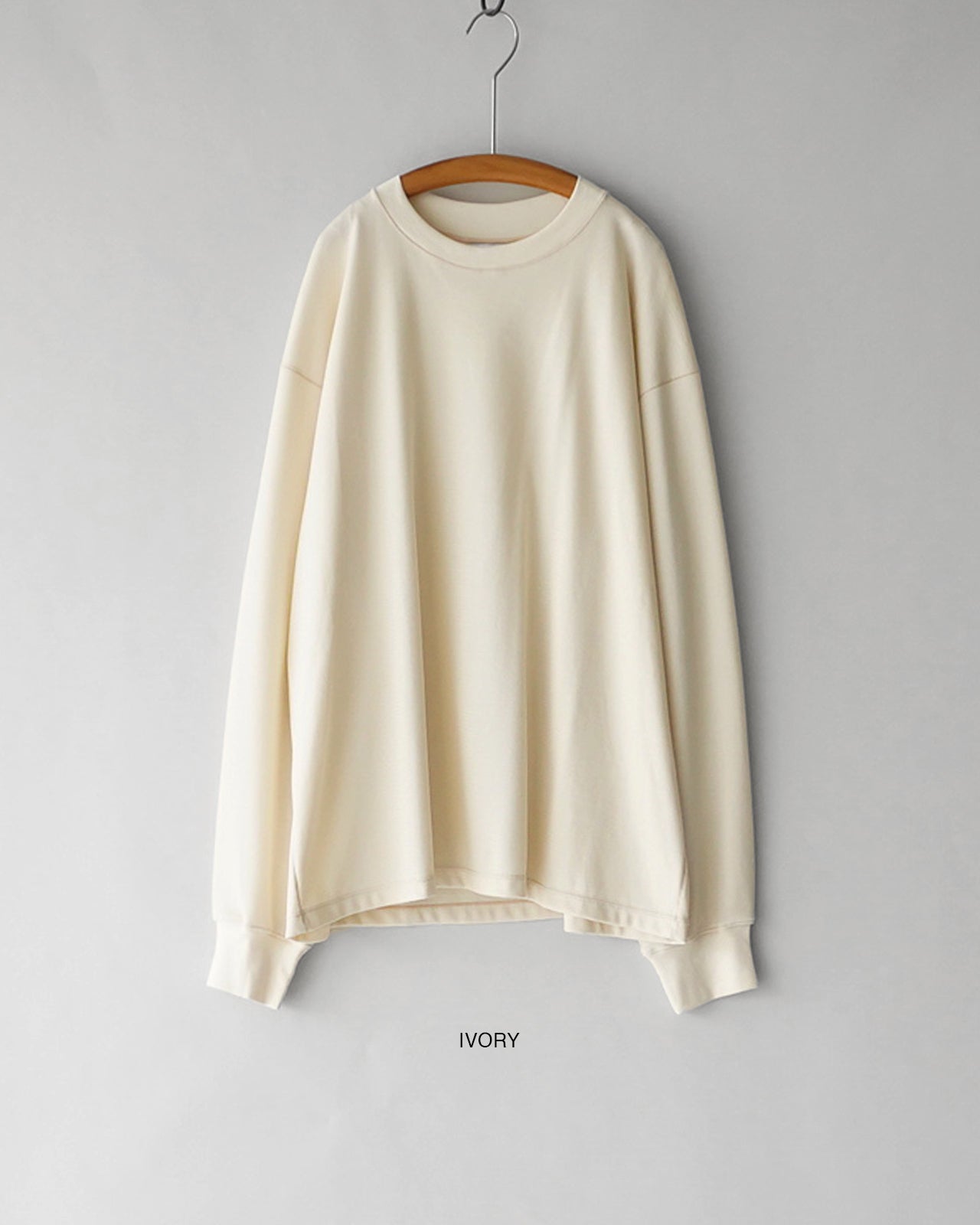 アイボリーカラーの長袖Tシャツ。胸元や袖口のディテールはシンプルで、裏地はやや光沢感のあるサーマル地の質感が感じられる画像。 hanger に掛けられた状態で、肩幅と着丈のバランスが分かるクリーンな印象。