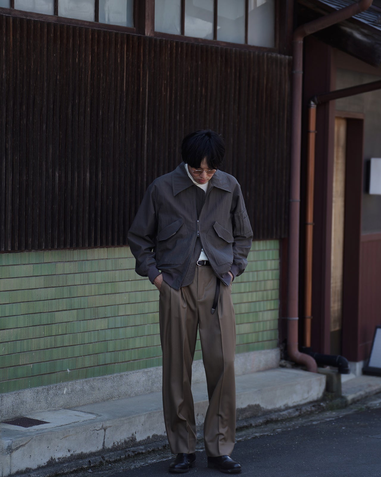 グレーのVeiled Flight Jacket RM262-010を着用した男性の全身写真。やや斜め前方を向き、前のポケット付きデザインと風合いのあるリップストップ生地が際立つ立ち姿。