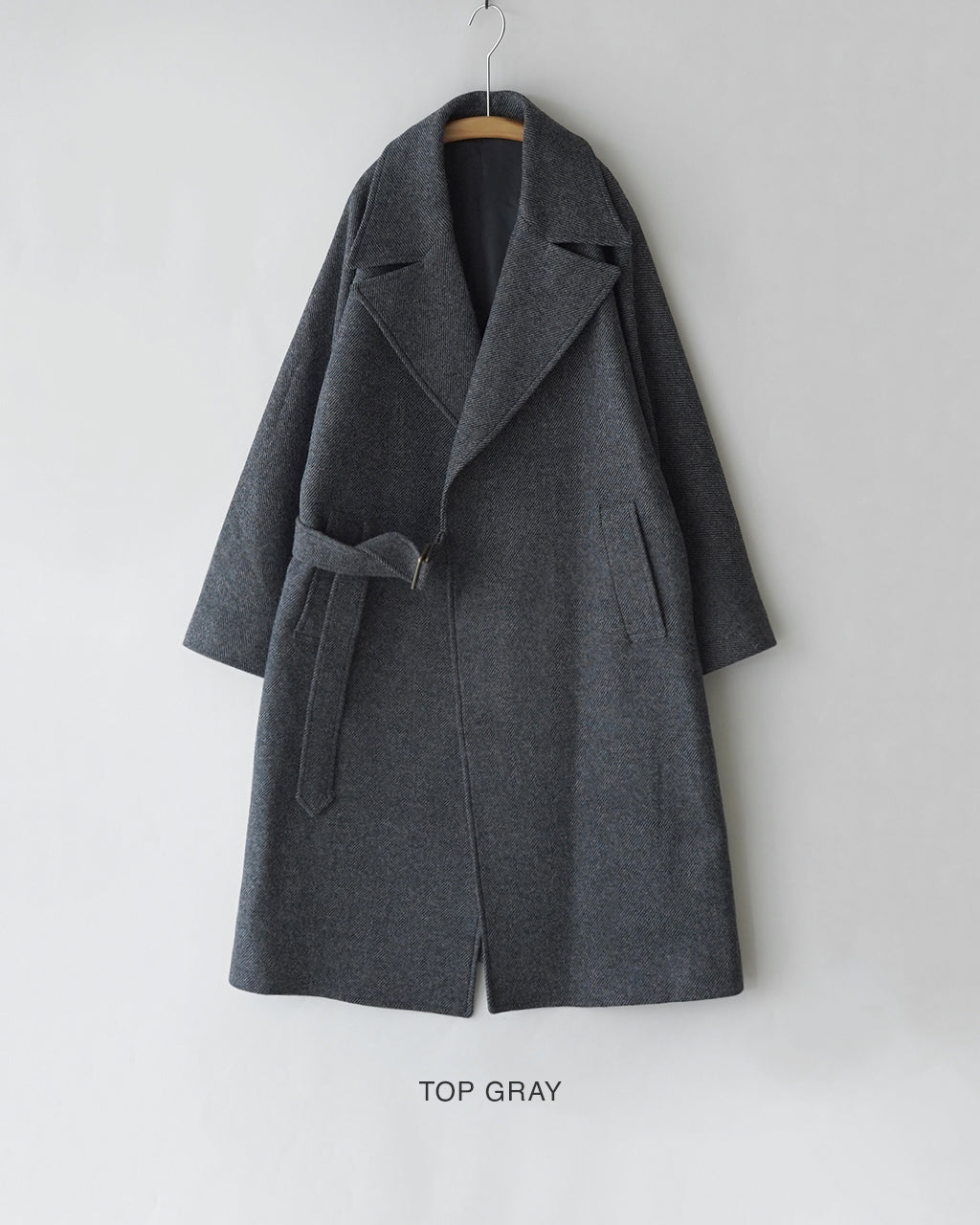 グレーメランジのウール混素材で作られたWRAP COATの正面ショット。大柄なラペルと共布ベルトが特徴で、腰まわりに緩やかなドレープを生むシルエットが確認できます。