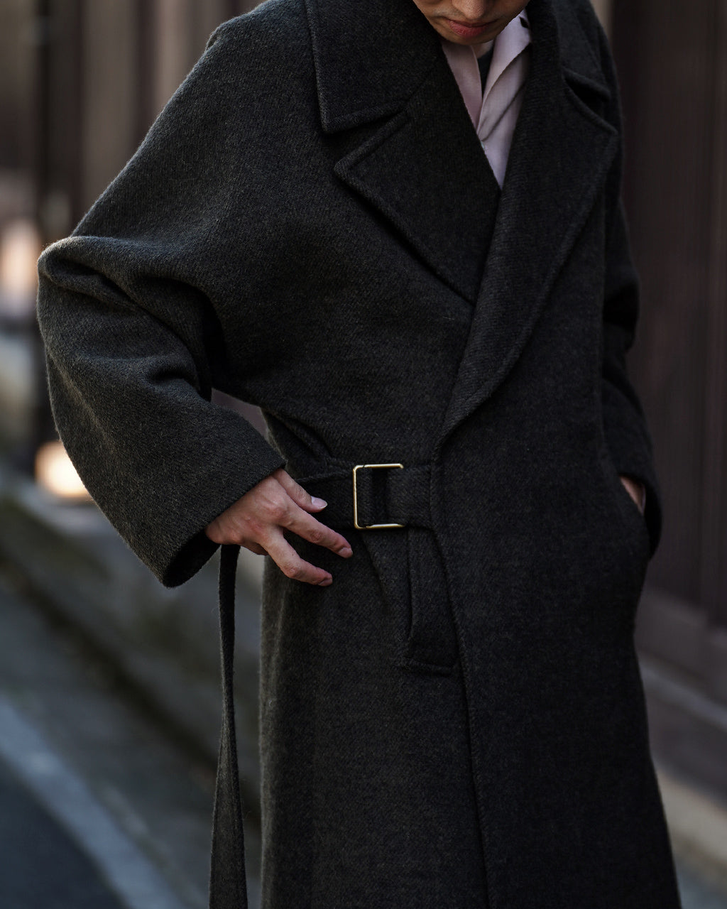 ダークグレーのWRAP COAT RM262-034を正面から着用したモデル。太めの幅広ベルトとウエストマークが特徴で、コートの大きなラペルと一枚布の美しいドレープが目を引くディテール。
