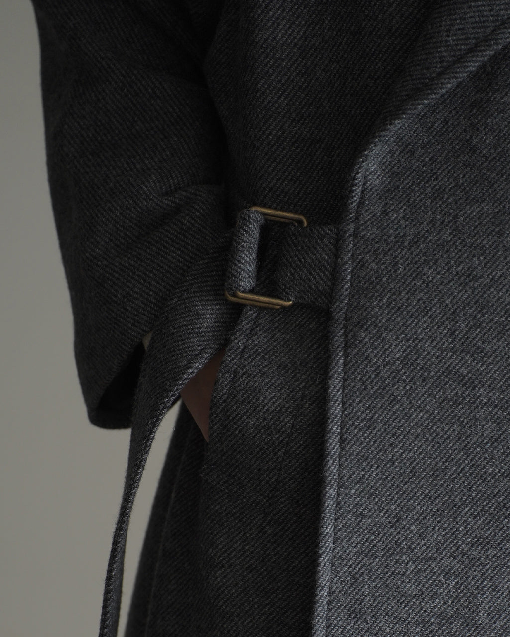 グレー系の二重織りウール生地のWRAP COAT RM262-034の袖口近く。留め具は brass色の金具で、布地が厚く重厚感のある質感が伝わるディテールショット。