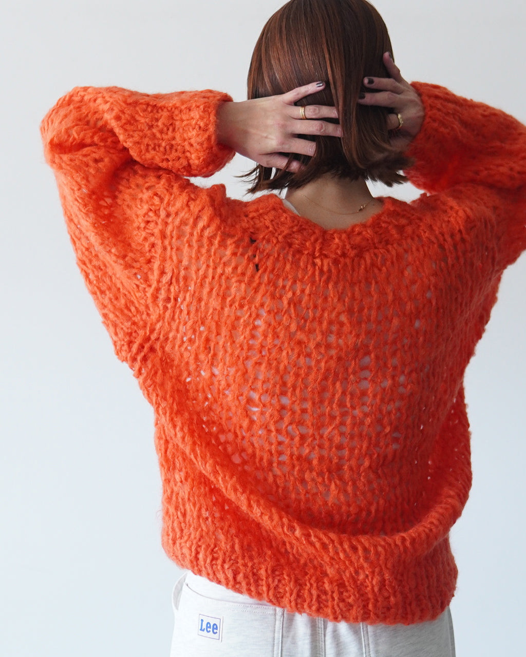 オレンジ系のざっくり編みが特徴のREEVES SWEATER。背中の開きのある透かし編みとボリューム袖が印象的で、クルーネックのリラックスシルエットを表現しています。