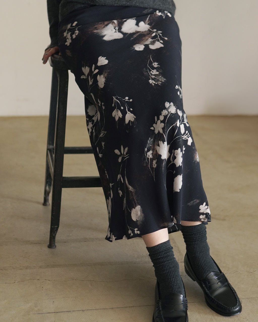 黒地に淡い花柄を重ねたロングスカート。裾まで落ちるナローラインで動きに沿うドレープ感が写真下で分かる。シルエットはすっきりとした印象。