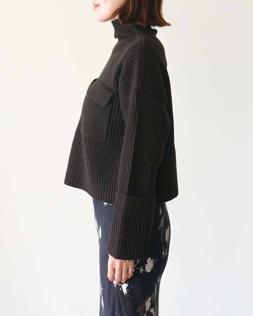 黒いボリューム感のあるタートルネックニット。ゆったりした身幅と長めの袖口、前面ポケットが特徴的なデザインです。