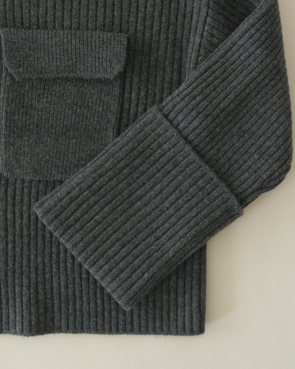 SACRAのBoiled Lambwool Rib Knitのディテールショット。濃いグレーのリブ編み生地と縫い目を近くで捉え、袖口と襟周りの質感がわかる拡大画像。