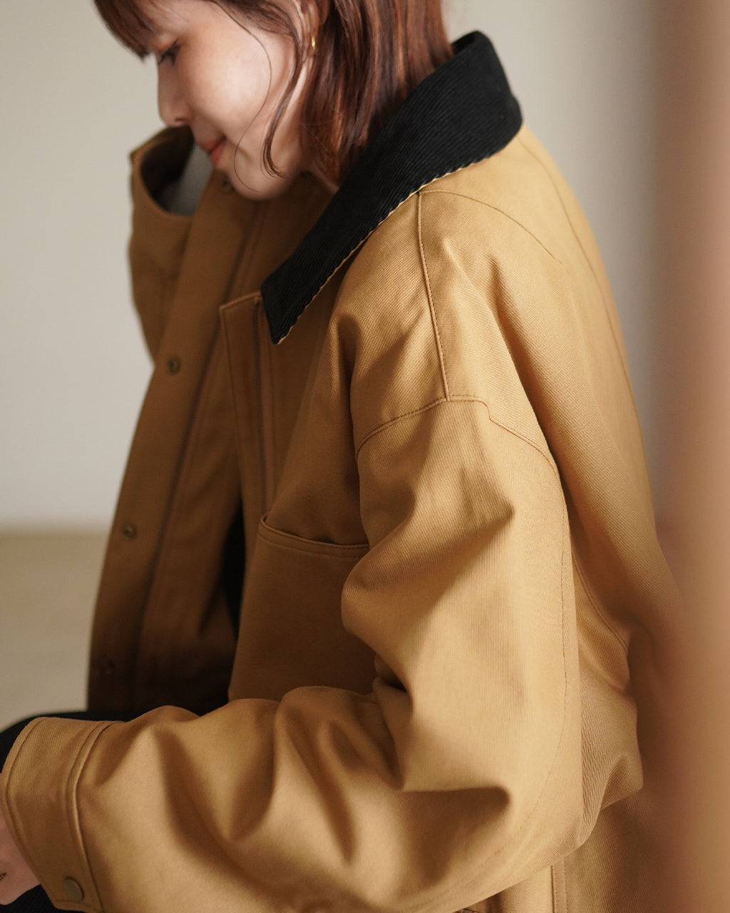 ベージュのCAVALRY TWILL JACKETの横姿。黒いカラーの襟がコントラストとなり、ゆったりとしたオーバーシルエットとコットンツイル生地の質感が見える。